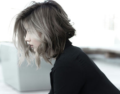 A woman sitting in profile view, with healthy, blonde-coloured curly hair covering her face.